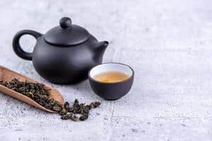 10798479-the-chaud-dans-une-theiere-noire-et-des-tasses-et-des-feuilles-de-the-seches-sur-fond-de-ciment-gris-clair-gros-plan-concept-de-conception-d-espace-de-copie-gratuit-photo